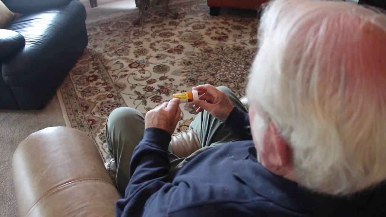 Man sitting in a chair taking medication from a bottle